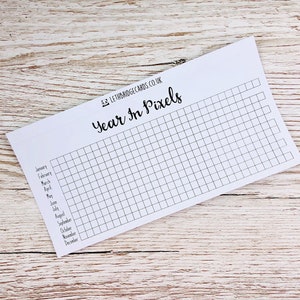 May include: A white printable year in pixels tracker with a grid of squares and a list of months from January to December. The text "Year in Pixels" is written in black cursive font. The text "Letbridgecards.co.uk" is written in black font.