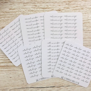 Op de afbeelding: Een set witte sticker vellen met zwarte handgeschreven tekst. De vellen bevatten de woorden "volgende week", "vandaag", "schoonmaken", "deze week" en "te doen".