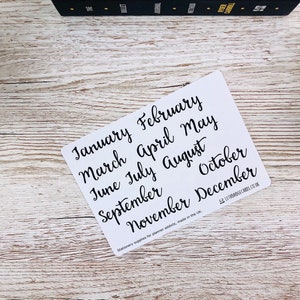 May include: White card with black handwritten text listing the months of the year: January, February, March, April, May, June, July, August, September, October, November, December. The text "Stationery supplies for planner addicts, made in the UK" is printed at the bottom of the card.