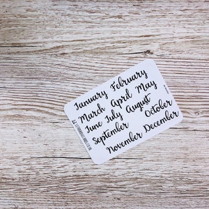 May include: A white card with the months of the year written in black cursive script. The months are January, February, March, April, May, June, July, August, September, October, November, and December.