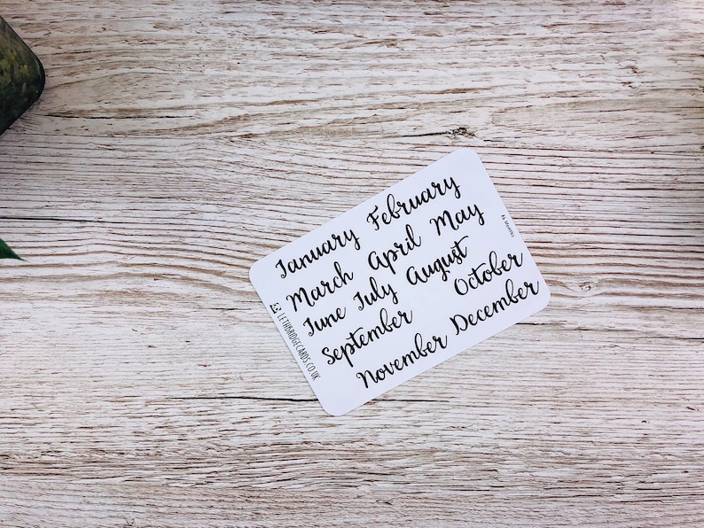 May include: A white card with the months of the year written in black cursive script. The months are January, February, March, April, May, June, July, August, September, October, November, and December.