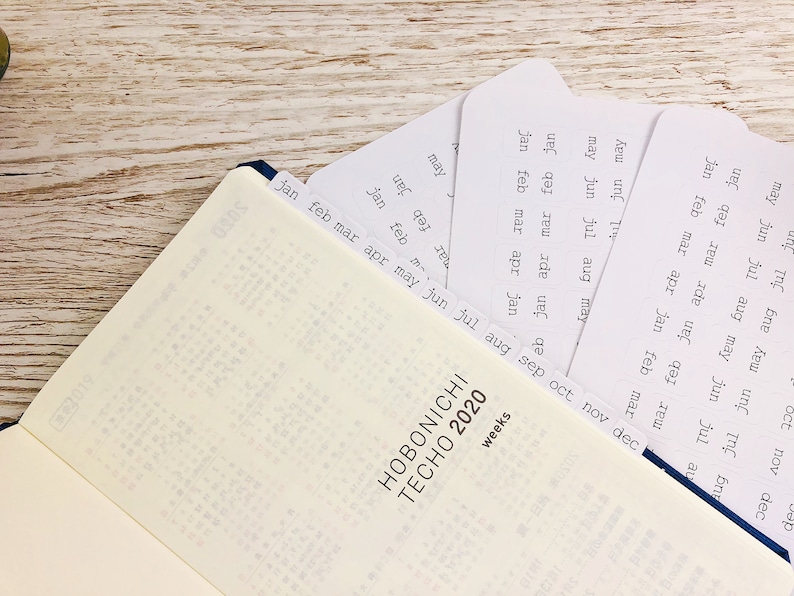 May include: A Hobonichi Techo 2020 weekly planner with a blue cover and white pages. The planner has a set of tabs for each month of the year, labelled with the month and the abbreviation for the month.