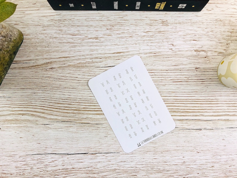 May include: A white card with the months of the year written in black ink. The card is on a light wood surface. The text "LETRBRIDGE CARDS CO.UK" is printed in the bottom right corner.