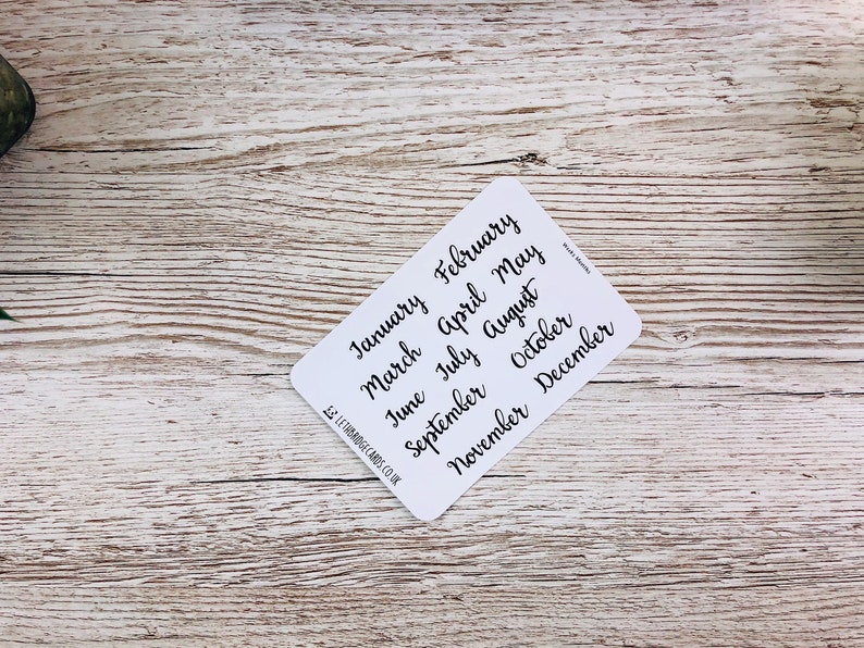May include: A white card with the months of the year written in black cursive script. The months are: January, February, March, April, May, June, July, August, September, October, November, December.