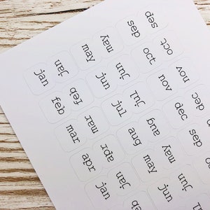 May include: White sticker labels with the months of the year written in black text. The labels are arranged in a grid pattern.
