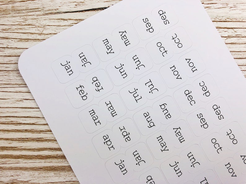 May include: White sticker labels with the months of the year written in black text. The labels are arranged in a grid pattern.