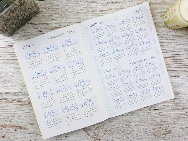 K&ouml;nnte beinhalten: Ein wei&szlig;es und cremefarbenes Kalenderbuch mit Monatskalendern f&uuml;r die Jahre 2019, 2020 und 2021. Das Buch ist auf den Kalender 2020 ge&ouml;ffnet.
