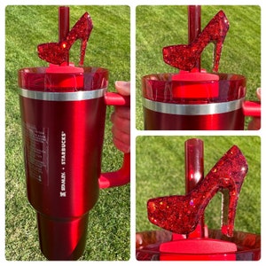 May include: Red stainless steel travel mug with a red high heel shoe straw topper. The mug has the text "Stanley + Starbucks" on the side.
