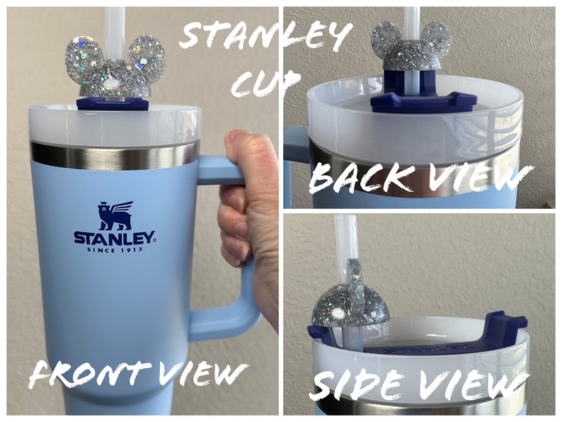 May include: A light blue Stanley travel mug with a black bear logo and the text "Stanley Since 1913". The mug has a handle and a white lid with a silver glitter Mickey Mouse ear lid topper and a straw.