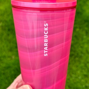 May include: A pink swirl tumbler with a Mickey Mouse lid and straw. The tumbler has the Starbucks logo on the side.