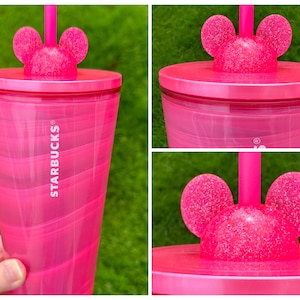 May include: Pink Starbucks tumbler with a glittery Mickey Mouse lid and a straw. The tumbler has a swirl design and the Starbucks logo is printed on the side.