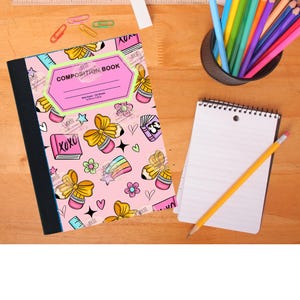 May include: A pink composition book with a black spine, decorated with yellow bows, pencils, and hearts. A spiral notebook with a pencil, a cup of coloured pencils, and stationery are on a wooden surface.