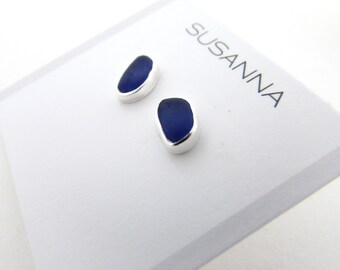 May include: A pair of silver earrings with blue sea glass stones. The earrings are on a white card with the word "SUSANNA" printed on it.