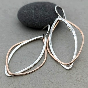 May include: A pair of silver and rose gold earrings with a hammered finish. The earrings are shaped like an oval with a smaller oval inside.