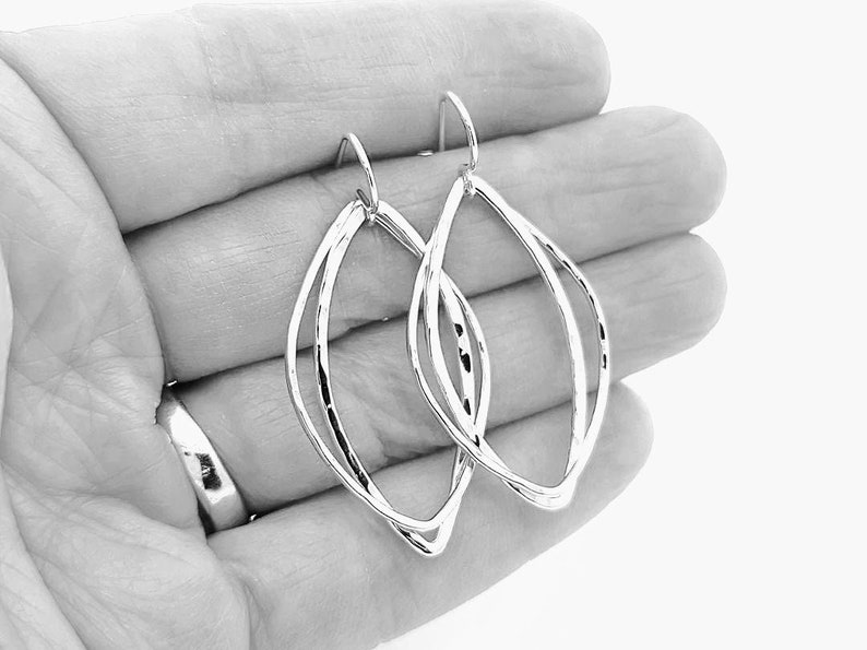 May include: Silver earrings with a double loop design. The earrings are made of a smooth, shiny metal and have a simple, elegant style.