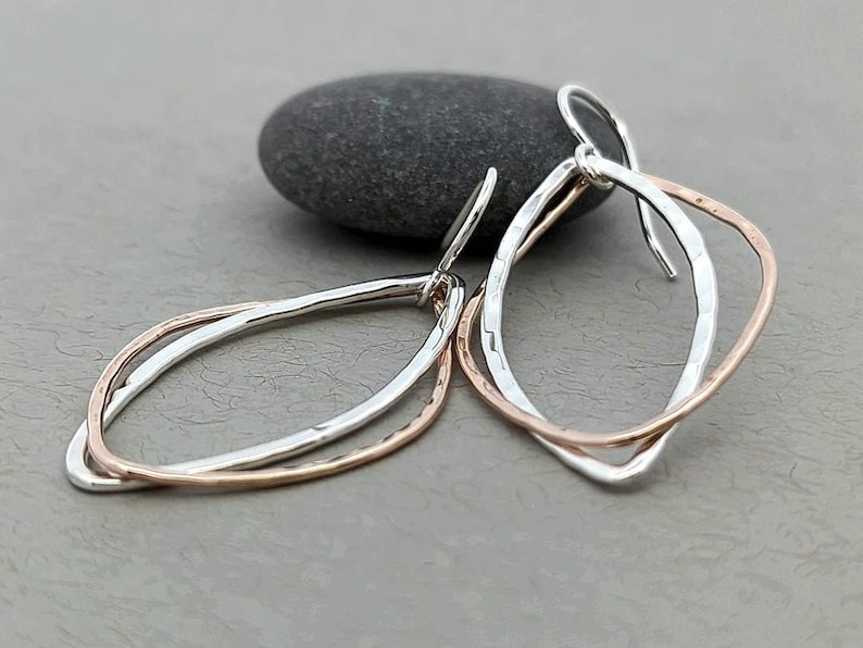 May include: A pair of silver and rose gold earrings with a simple, organic shape. The earrings are made of two overlapping loops, one silver and one rose gold.