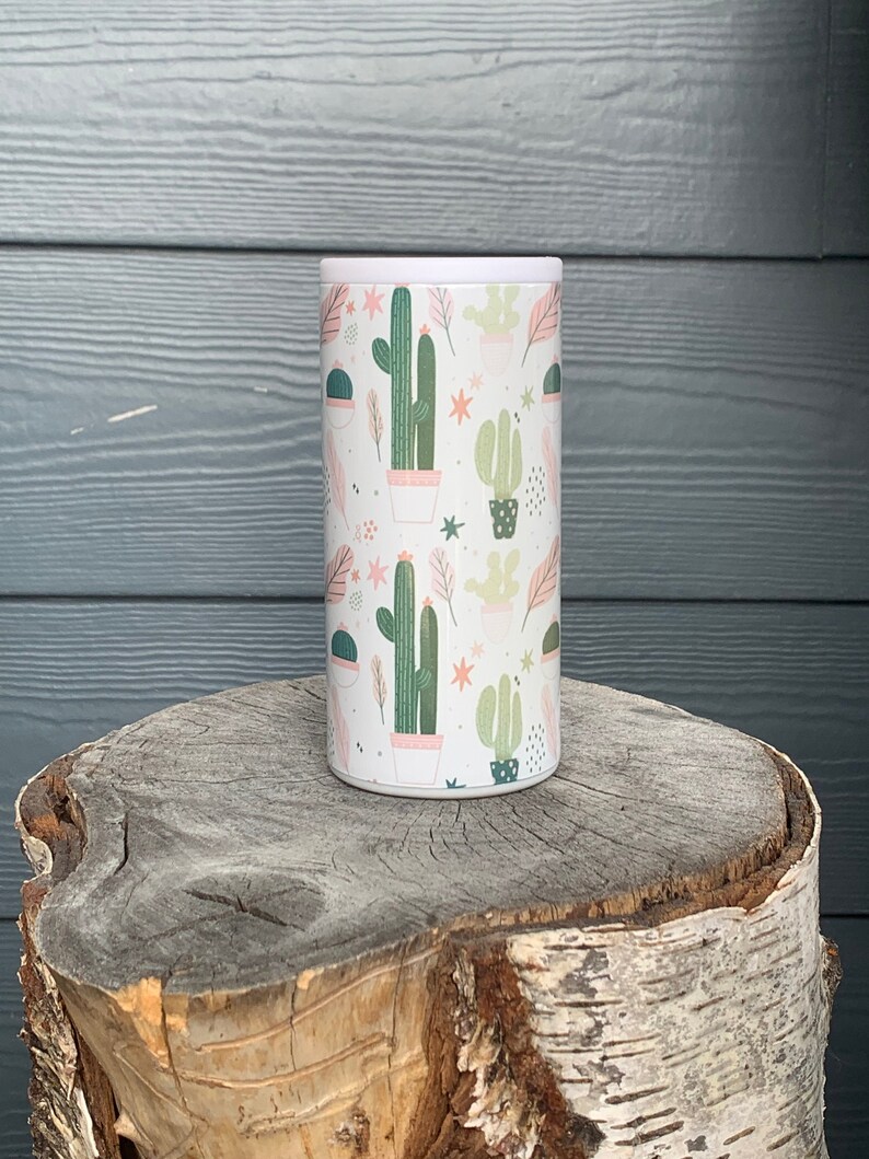 Op de afbeelding: Een witte ge&iuml;soleerde beker met een roze en groene cactusprint. De beker heeft een wit deksel.