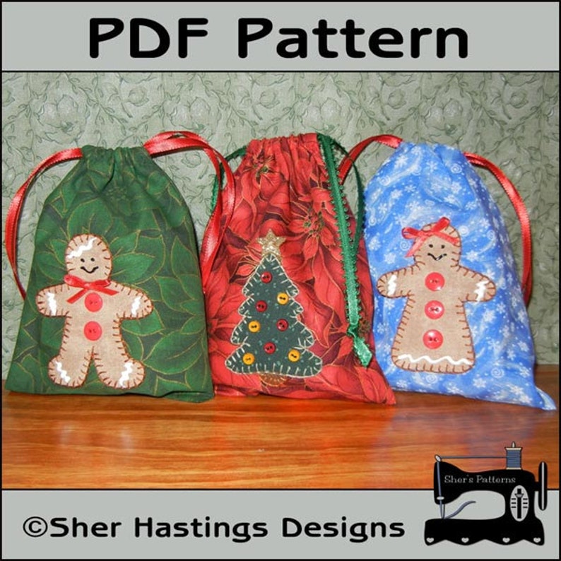 May include: Three Christmas-themed fabric gift bags with drawstring closures. The bags are decorated with a gingerbread person, a Christmas tree, and snowflakes. The bags are on a wooden surface. Sher Hastings Designs is printed on the bottom of the image.