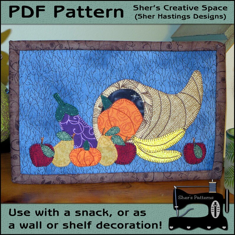 May include: A PDF pattern for a quilted cornucopia with fall fruits and vegetables. The cornucopia is filled with a pumpkin, pears, apples, and an eggplant. The background is a blue fabric with a brown border.