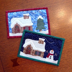 K&ouml;nnte beinhalten: Zwei gesteppte Untersetzer zum Thema Weihnachten. Der erste Untersetzer zeigt ein braunes Haus mit einem wei&szlig;en Dach und einem gr&uuml;nen Baum. Der zweite Untersetzer zeigt ein braunes Haus mit einem wei&szlig;en Dach und einen Schneemann.