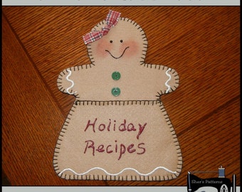 May include: A tan felt gingerbread person with a stitched outline and the words "Holiday Recipes" embroidered in red. It has a red and white plaid bow, green button eyes, and a stitched smile. The text "PDF Pattern" is at the top.