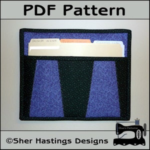 May include: A wall-mounted fabric organizer with three pockets for storing files. The pockets are labeled "Prospects - In Line", "Recent Deliveries", and "General Info". The organizer is made of a dark green fabric with a light blue and purple floral pattern.