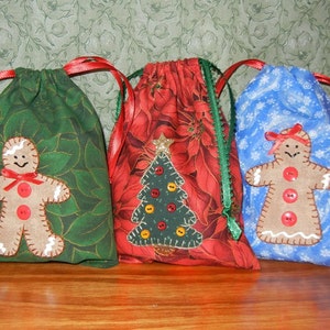 May include: Three Christmas gift bags with different designs. The first bag is green with a gingerbread person, the second is red with a Christmas tree, and the third is blue with a gingerbread person.
