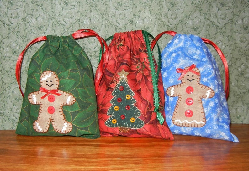 May include: Three Christmas gift bags with different designs. The first bag is green with a gingerbread person, the second is red with a Christmas tree, and the third is blue with a gingerbread person.