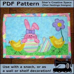 May include: A PDF pattern for a quilted wall hanging featuring a pink bunny holding an Easter egg, two yellow chicks, and a purple flower. The pattern is titled "Sher's Creative Space (Sher Hastings Designs)".