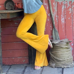 May include: A woman wearing a gray tank top with a white feather print and mustard yellow bell bottom pants.