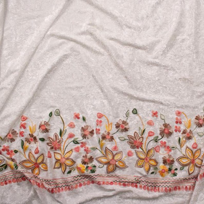 Pode incluir: Tecido branco com um design de bordado floral. O bordado apresenta uma borda de pequenas flores em tons de marrom, laranja e rosa.