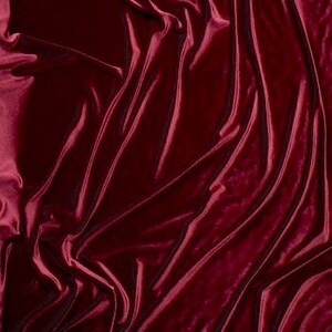 May include: Close-up of a deep red velvet fabric with a smooth, soft texture. The fabric is draped in folds, creating a luxurious and elegant look.