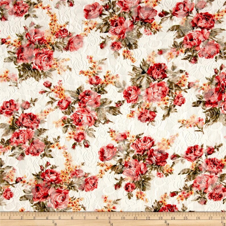 May include: White fabric with a floral pattern featuring red and pink roses. The fabric has a lace-like texture.