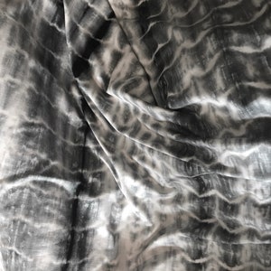May include: A close-up of a white and grey tie-dye fabric with a wavy pattern.