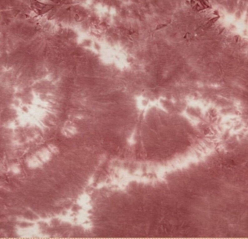 May include: A close-up of a red and white tie-dye fabric. The fabric has a swirling pattern of red and white.