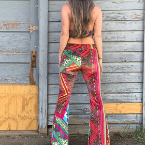 May include: A pair of wide-leg, bell-bottom pants with a colorful, geometric pattern. The pants are made of a soft, velvet-like fabric and have a high waist. The pants are pink, brown, yellow, blue, and green.