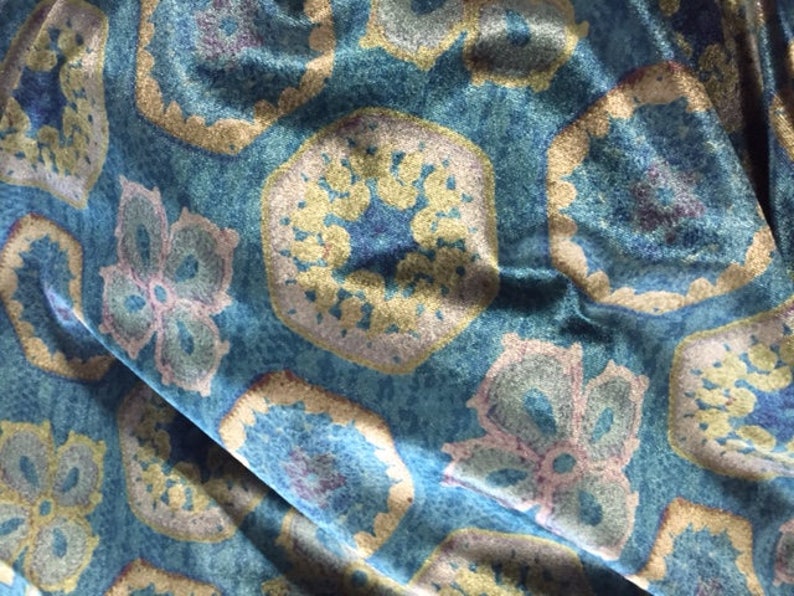 May include: Blue fabric with a repeating pattern of gold and pink floral designs. The fabric has a textured, velvet-like surface.