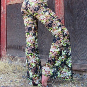 May include: Black lace pants with a floral print in shades of green, brown, and white. The pants have a wide leg silhouette.