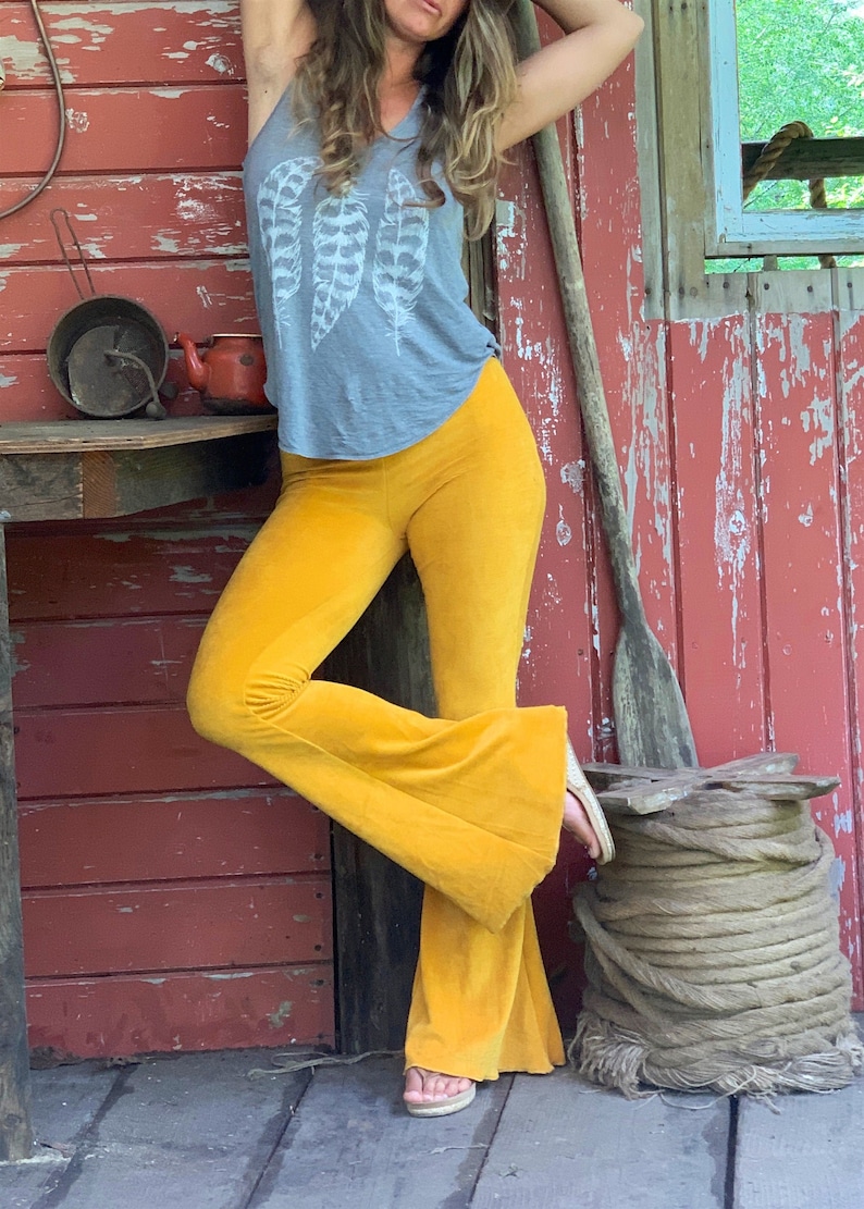 May include: A woman wearing a gray tank top with a white feather print and mustard yellow bell bottom pants.