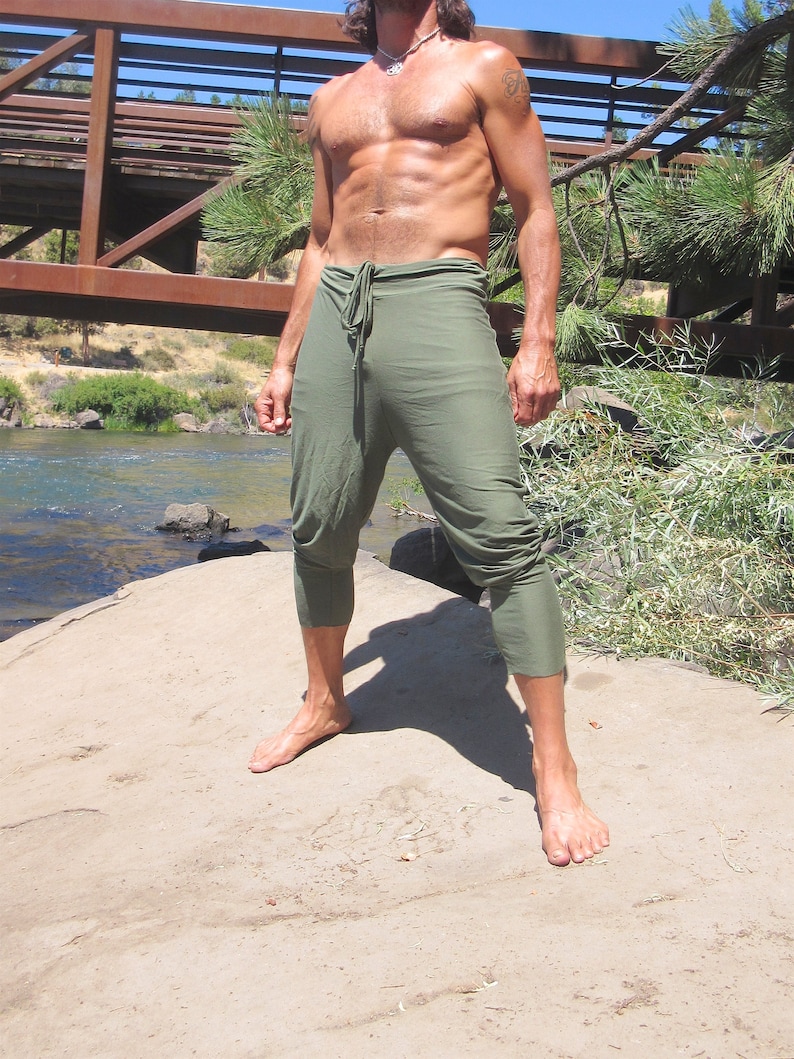 May include: A man wearing a pair of olive green trousers with a drawstring waist. The trousers are loose fitting and have a wide leg.
