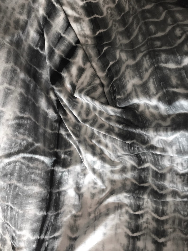May include: A close-up of a white and gray tie-dye fabric with a wavy pattern.