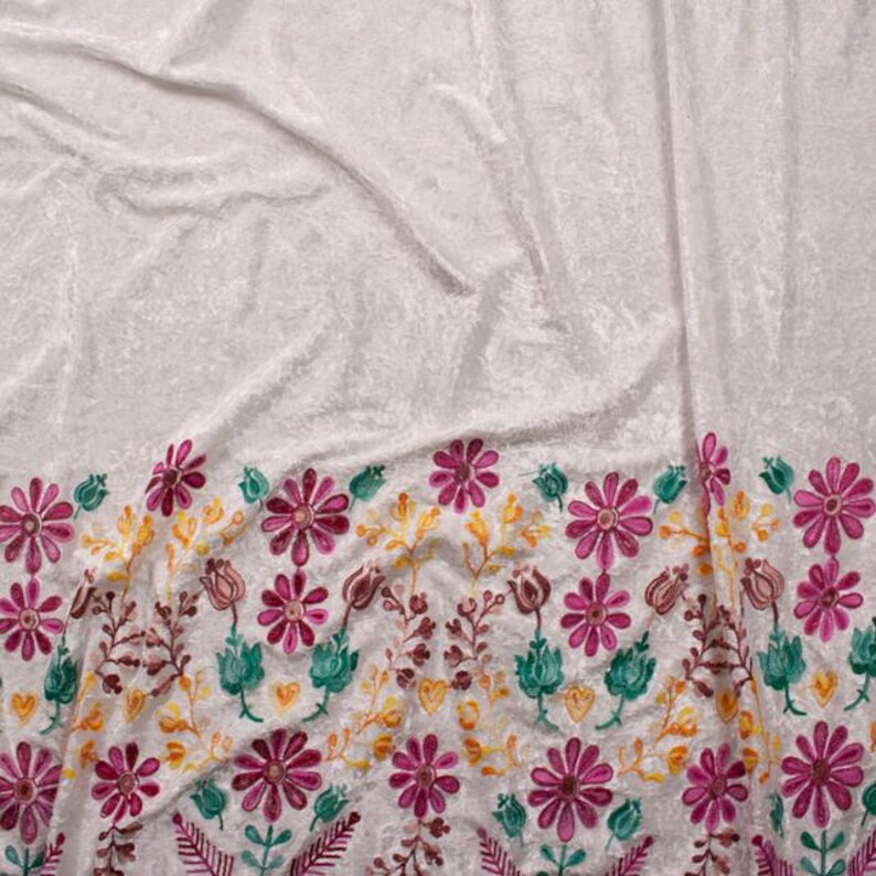 Pode incluir: Tecido de veludo branco com uma borda floral bordada em rosa, verde e amarelo.