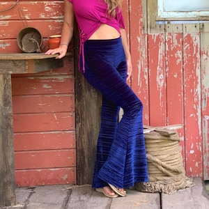 May include: A woman wearing a bright pink, one-shoulder top with a knot at the waist and blue velvet bell-bottom pants.