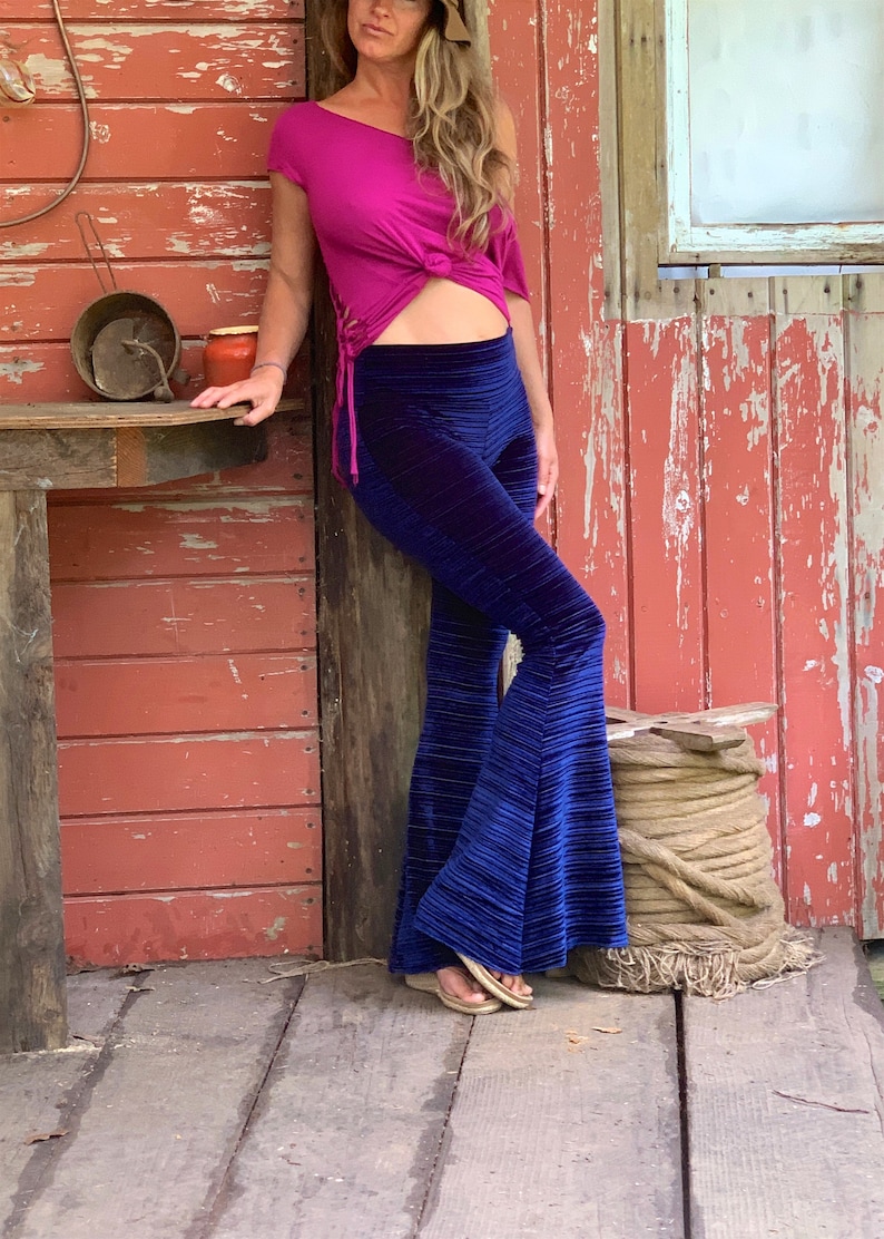 May include: A woman wearing a bright pink, one-shoulder top with a knot at the waist and blue velvet bell-bottom pants.