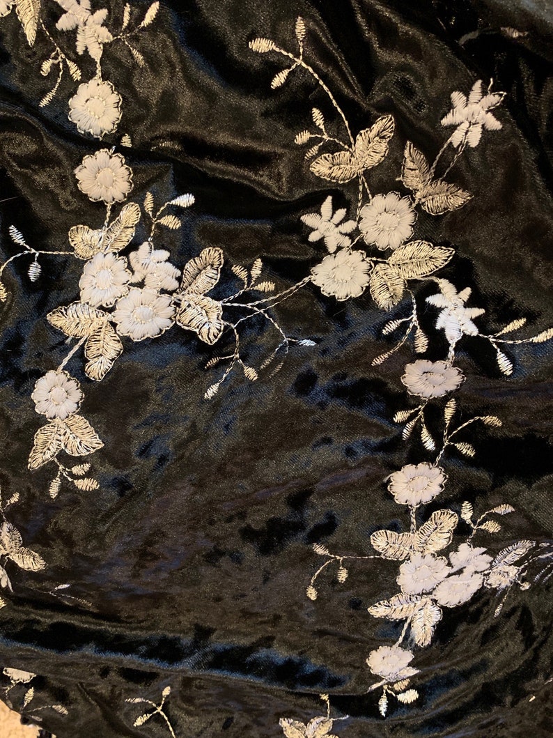 Pode incluir: Tecido de veludo preto com desenhos florais bordados em branco. O tecido tem uma textura macia e felpuda.