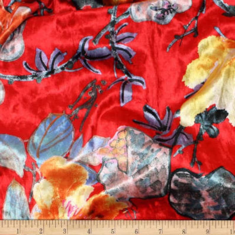 K&ouml;nnte beinhalten: Roter Samtstoff mit einem floralen Druck in Blaut&ouml;nen, Gelb und Orange. Der Stoff hat ein weiches, luxuri&ouml;ses Gef&uuml;hl und ist perfekt f&uuml;r Bastelprojekte.
