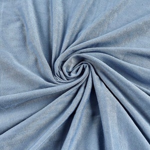 May include: A close-up of a light blue fabric with a soft, smooth texture. The fabric is folded and draped, creating a sense of movement and flow.
