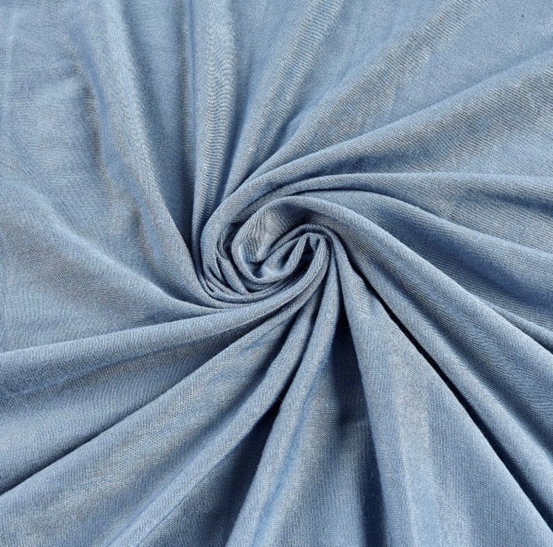 May include: A close-up of a light blue fabric with a soft, smooth texture. The fabric is folded and draped, creating a sense of movement and flow.