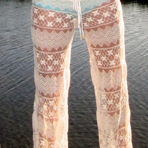 May include: White crochet pants with a delicate floral pattern. The pants are sheer and flowy, perfect for a beach day or a summer evening.