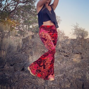 Puede incluir: Una mujer con un top negro sin mangas y pantalones acampanados de terciopelo con estampado paisley rojo y rosa. Los pantalones tienen una pierna ancha.